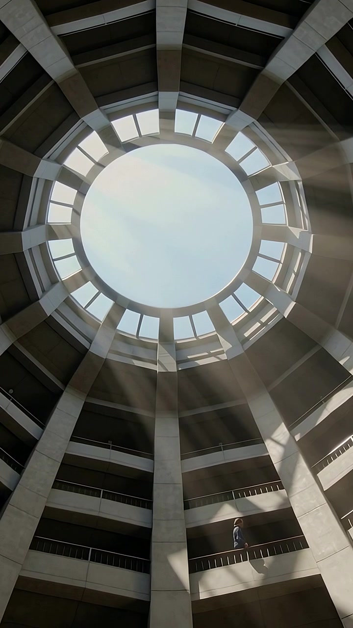 Vertical video: Panning camera showing jacketed man walking mid balcony in atrium, skylight beams