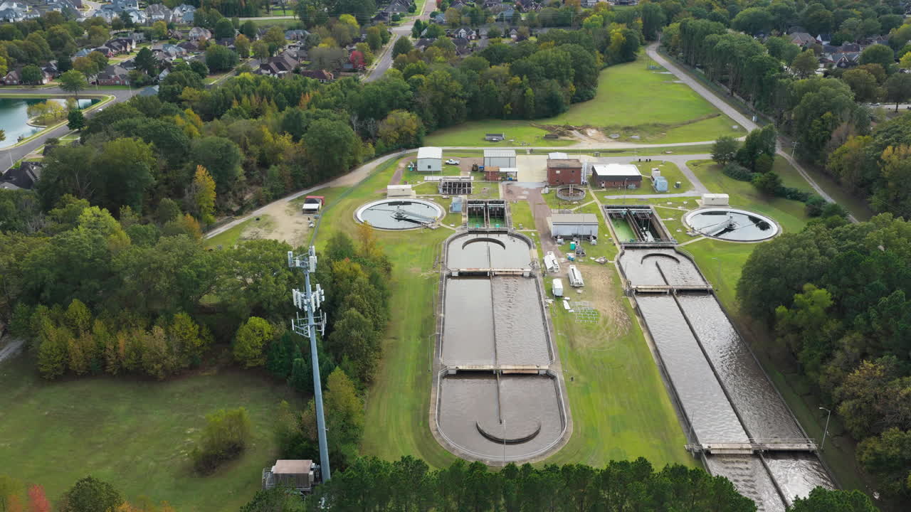 Aerial tracking left of wastewater treatment basins and infrastructure with pools spinning to remove chemicals, tilt up to community serviced