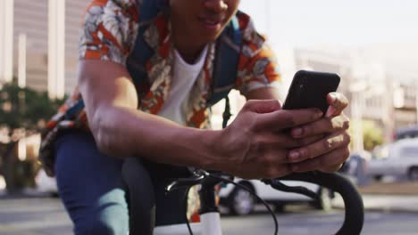 african american man in city, sitting on bike in street using smartphone