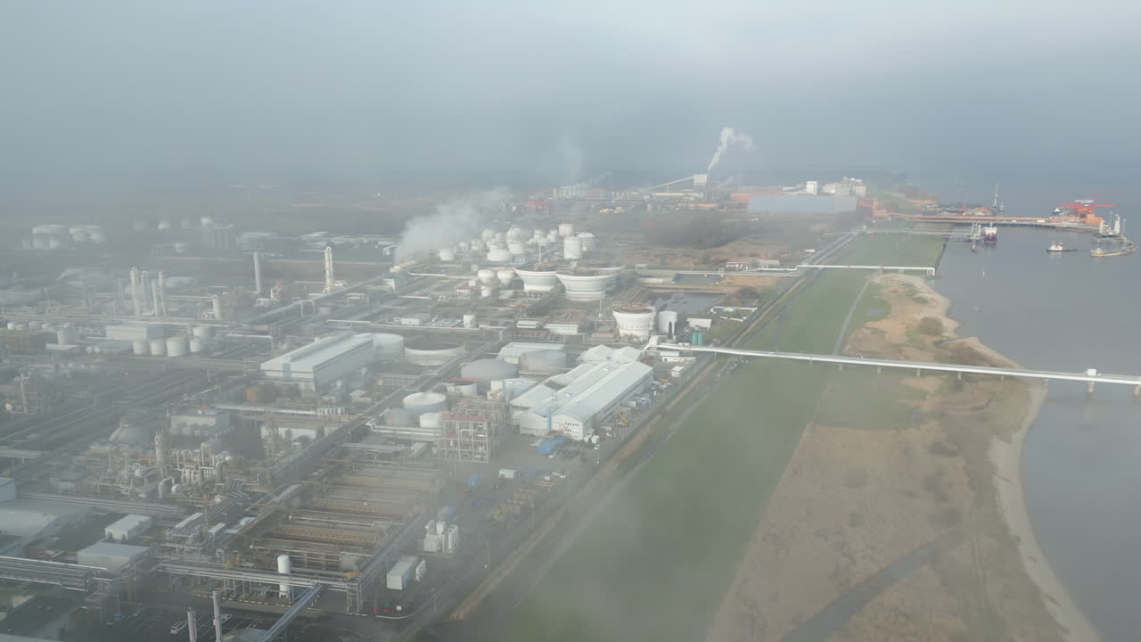 Smoke and steam rising of an industrial facility on a river, CO2 emissions, air pollution, exhaust gases, aerial, flight through steam