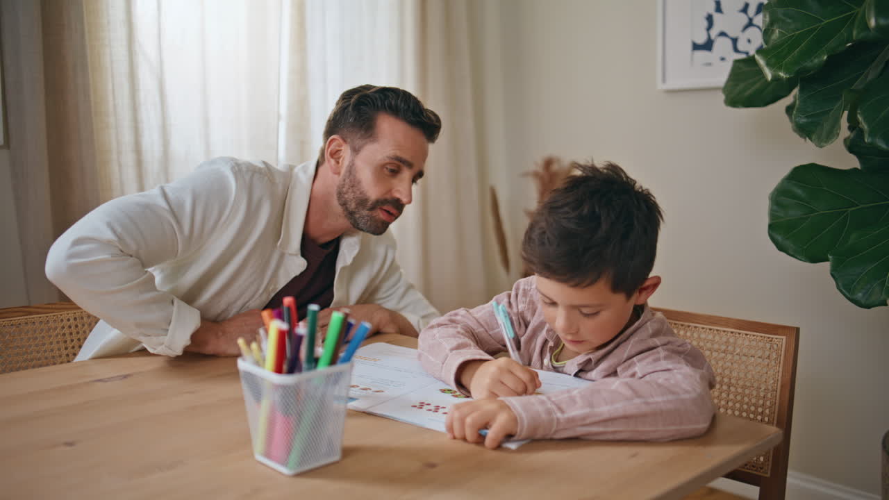 Closeup dad teaching boy doing homework in living room. Small child and parent