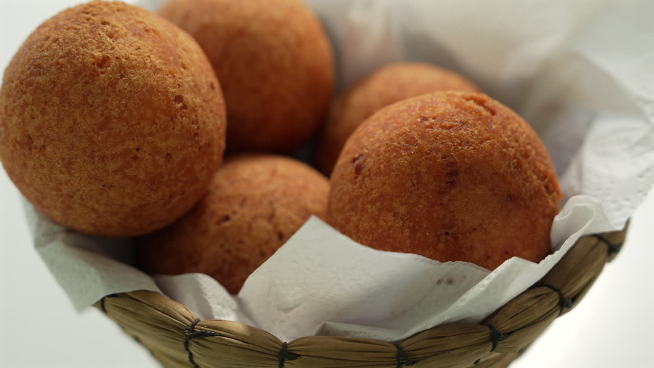 Close-up shot of golden buñuelos nestled in a basket lined with paper. Warm lighting enhances the crisp, fried texture, making it perfect for culinary and cultural themes
