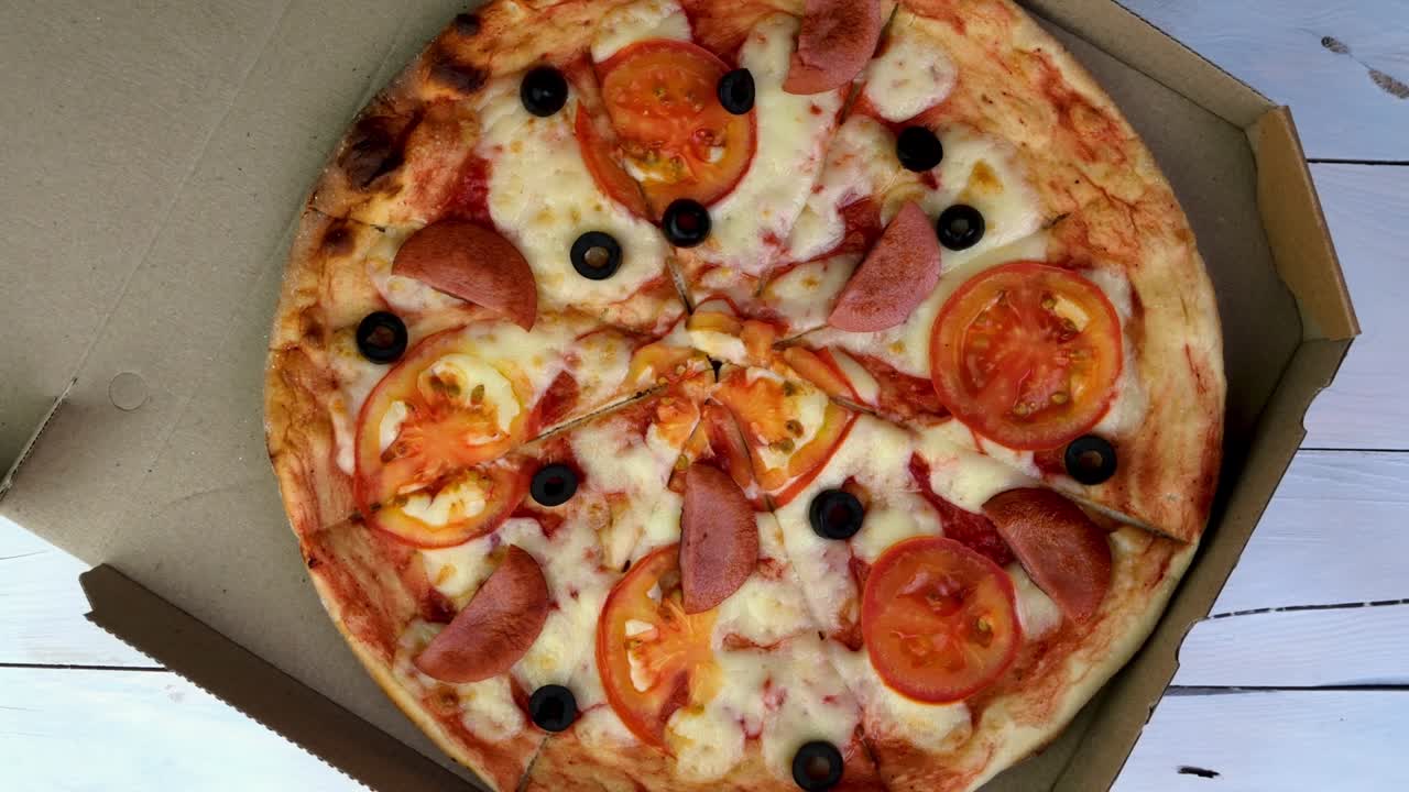 토마토, 소시지, 모차라, 올리브가 들어있는 신선한 둥근 피자는 천천히 회전합니다.