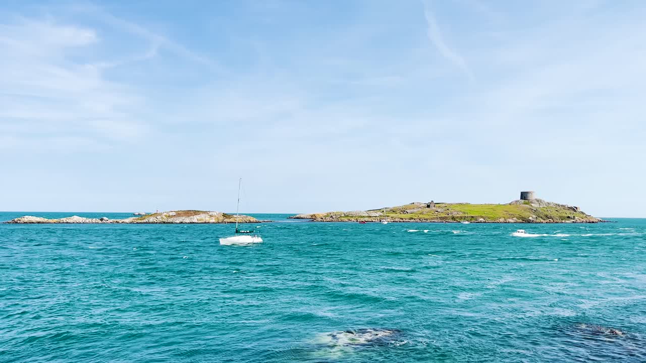 Dalkey Island with church ruin and martello tower in the distance on a beautiful sunny day. Boats slowly coming into the shore
