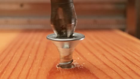 close-up is an electric drill the screws a self-tapping screw into a wooden bar.