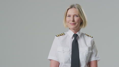 studio portrait of smiling mature female airline pilot or ship captain against plain background