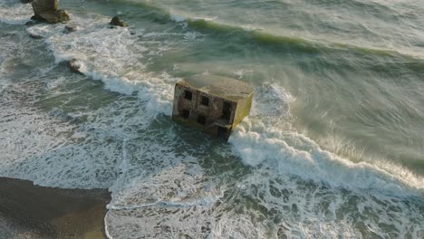 beautiful aerial establishing view of karosta concrete coast fortification ruins, sunny summer evening, golden hour light, stormy waves at baltic sea, slow motion birdseye drone orbit shot