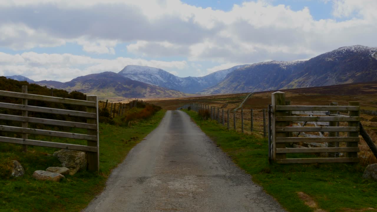 카메라는 영국의 웨일즈 산맥으로 이어지는 시골길이 있는 열린 문을 가로질러 추적합니다.