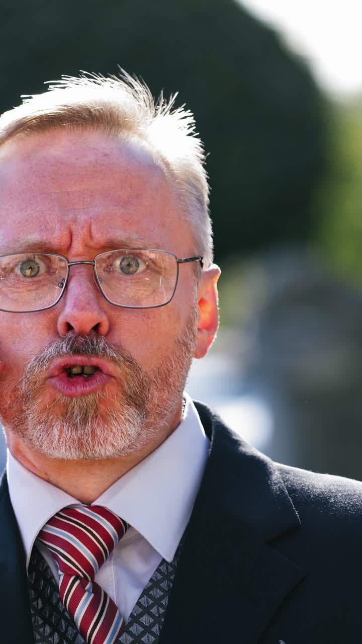 Close-up face of elderly man in eyeglasses talking on cellphone outdoors. Portrait of a handsome senior bearded businessman against city background. Vertical video