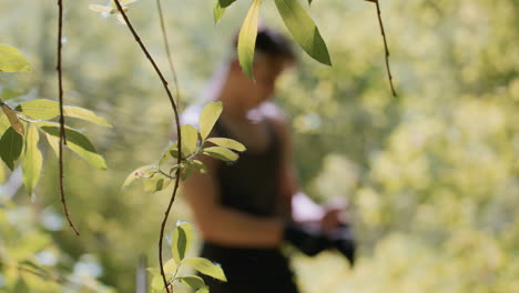 sharp focus on sunlit leaves in foreground with blurred adventurer adjusting fingerless gloves at waist in dense green forest preparing for next trek under dappled soft canopy light