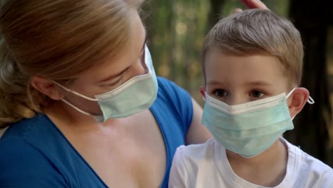 mother hugs her son in medical masks while sitting in a park 03