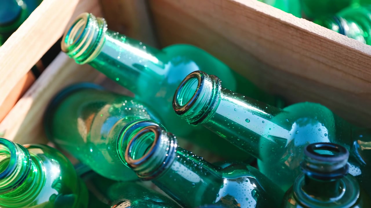 Primer plano de botellas de vidrio verdes descansando en una caja de madera, iluminadas por la cálida luz del sol que crea reflejos brillantes y gotas de agua visibles en las superficies