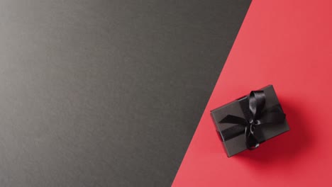 overhead view of black gift box black ribbon on black and red background with copy space