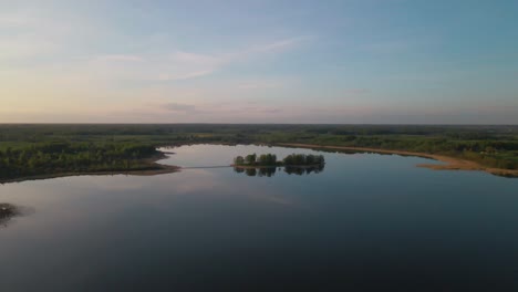 drone flies right, smoothly orbiting a small island on a calm lake, drawing closer to it.