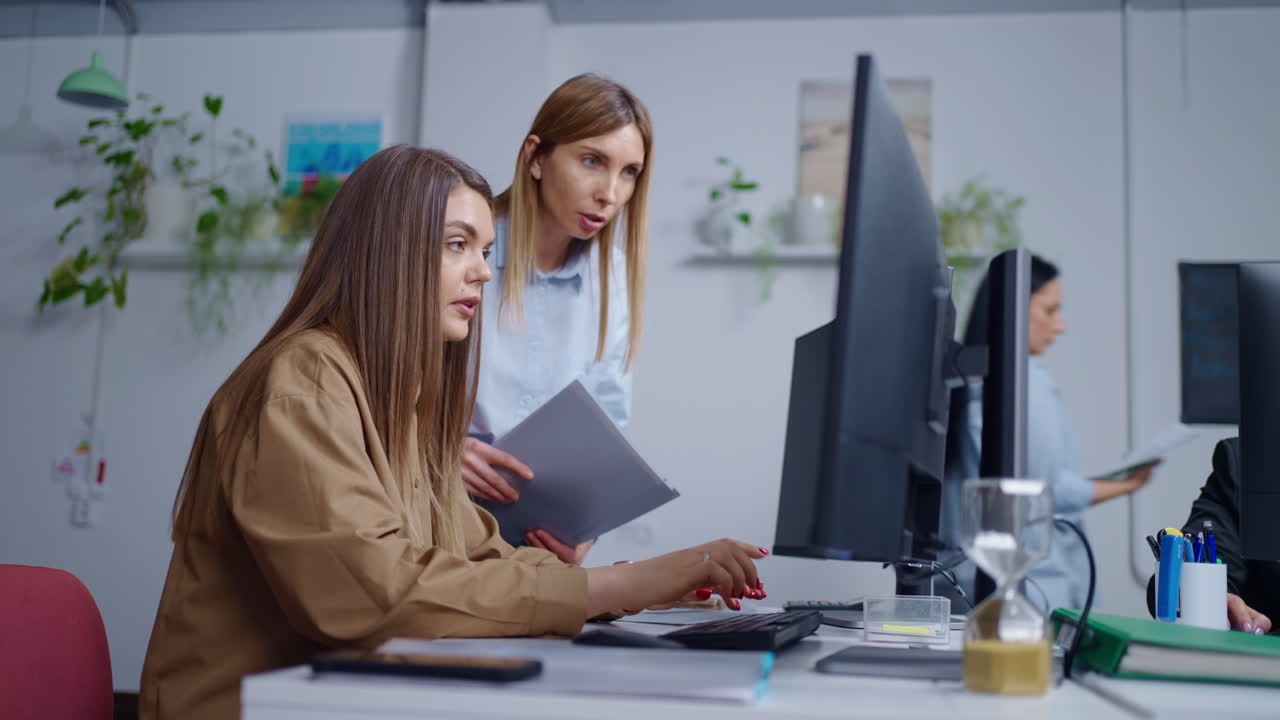Two women working on a computer in an office.