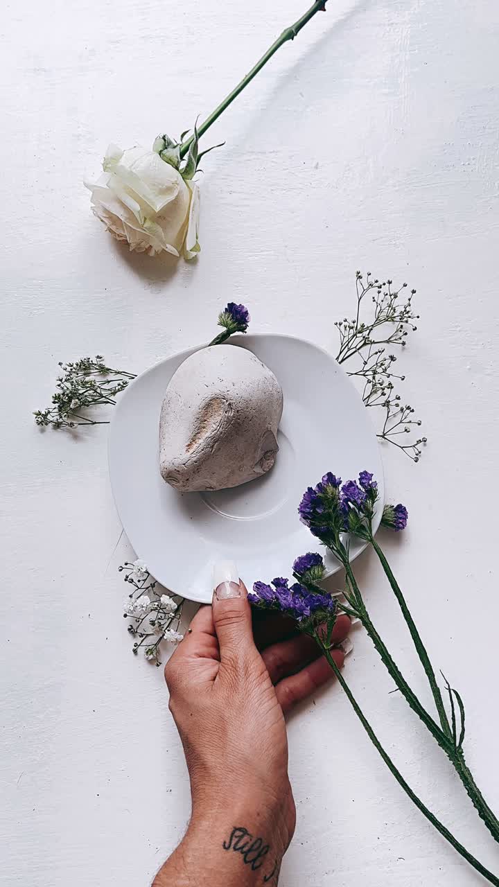 Elegant stilleben med blomster, en sten og en hånd