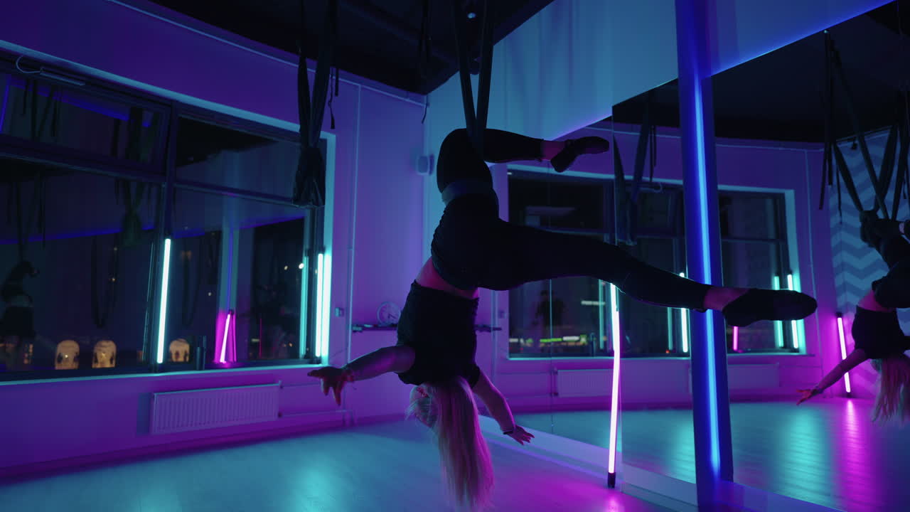 Woman hanging upside down and using yoga hammock swing while doing antigravity yoga exercise. Back view of beautiful young woman using hammock for doing pose of antigravity yoga