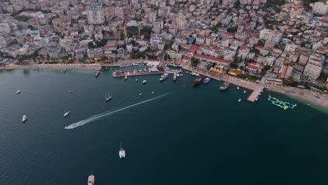 saranda, albania coastline at sunset with boats in the harbor and city in the background, aerial view