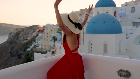 una turista con un vestido rojo disfruta de la vista del atardecer en el pueblo de oia, santorini