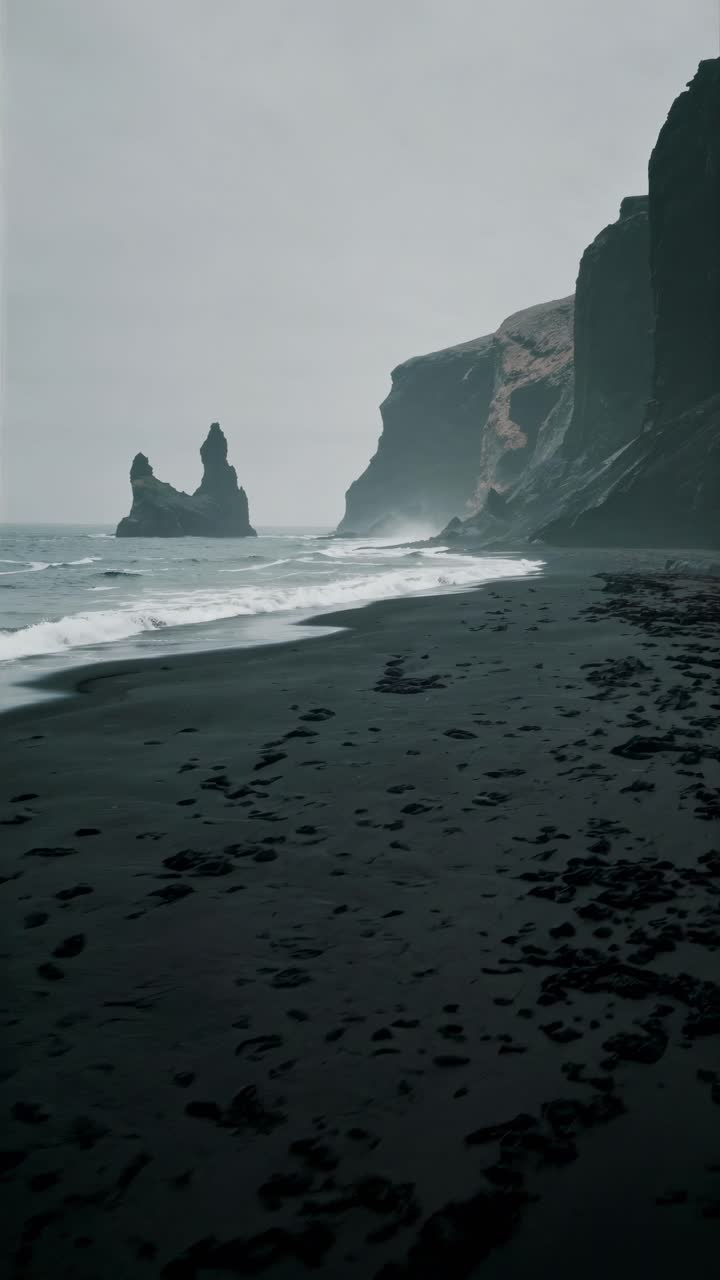 Moody seascape video concept with a low-angle view of a black sand beach, dramatic cliffs, and misty