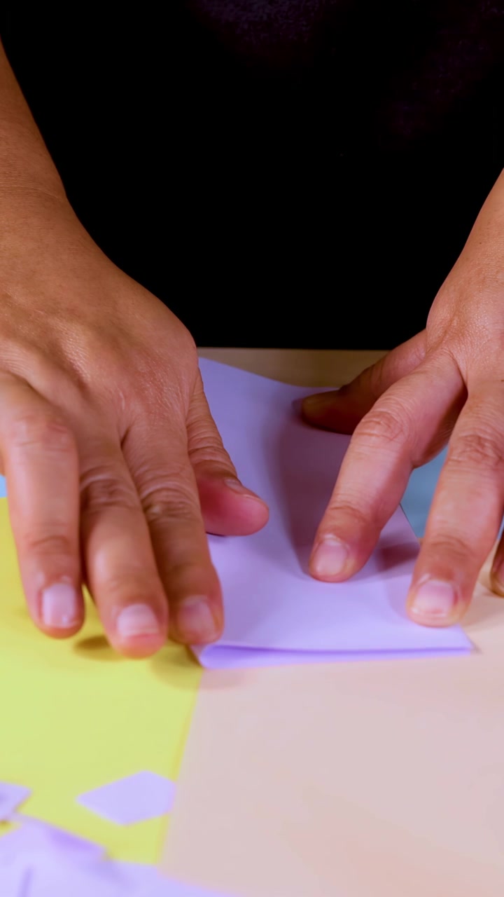Person’s hands carefully fold pastel paper on table, bright lighting, close-up, steady camera