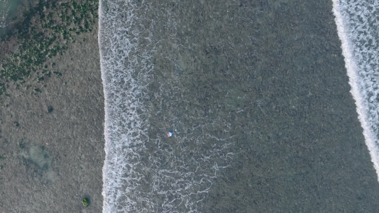 Top down descending drone shot over dead coral reef under shallow water with floating trash in tropical Balangan Beach Uluwatu Bali Indonesia