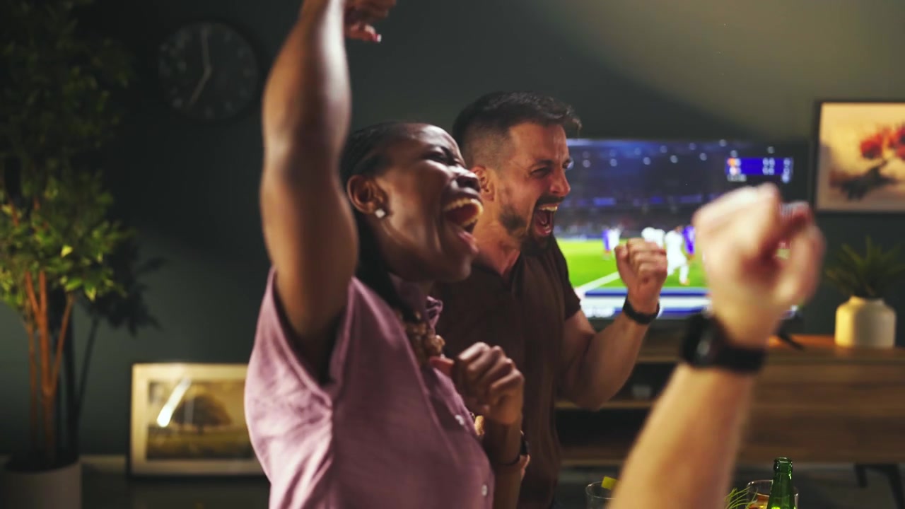 Amici di diverse origini che esultano guardando una partita di calcio in televisione a casa