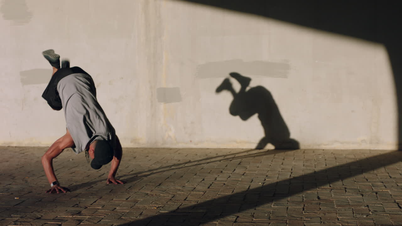 joven bailarín de break hombre bailando en la calle realizando varios movimientos de baile de estilo libre adecuado hombre de raza mixta practicando en la ciudad al atardecer con sombra en la pared