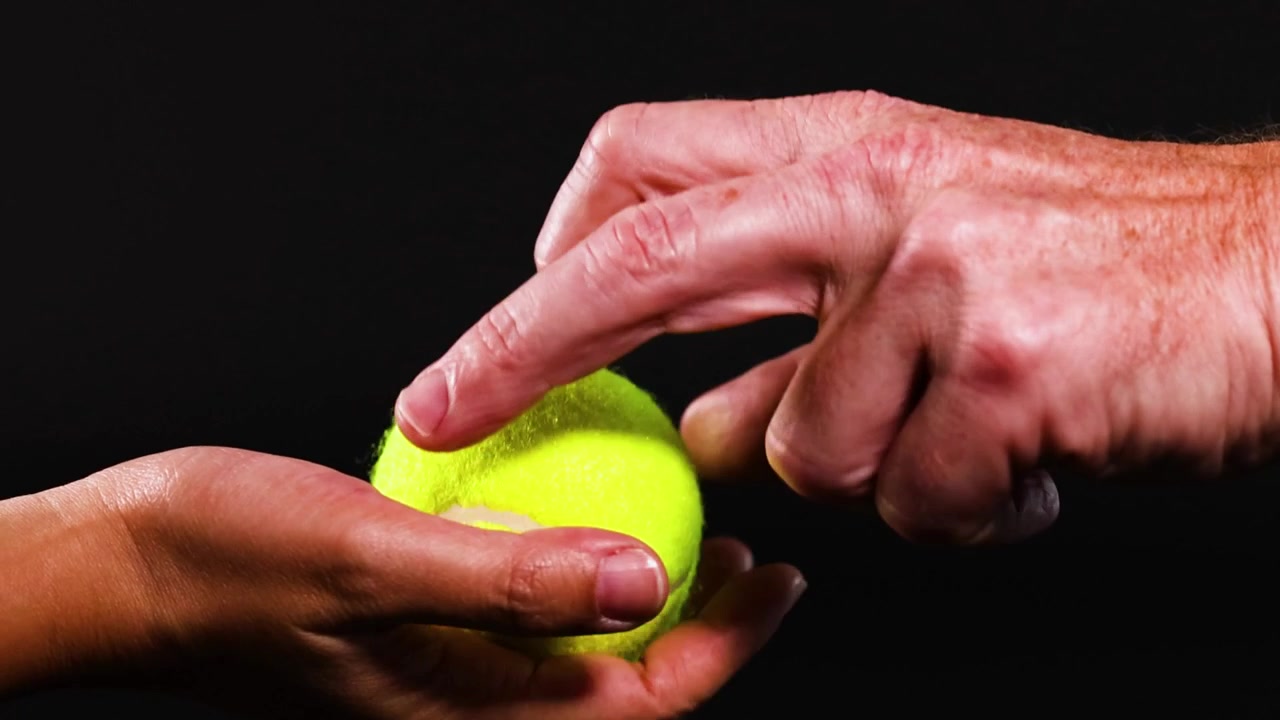 Close-up of hands exchanging a tennis ball against a black background, highlighting interaction and movement.