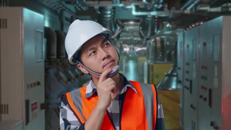 close up of asian male engineer with safety helmet thinking and looking around then raising his index finger while standing in engine control room, work of electrical generators