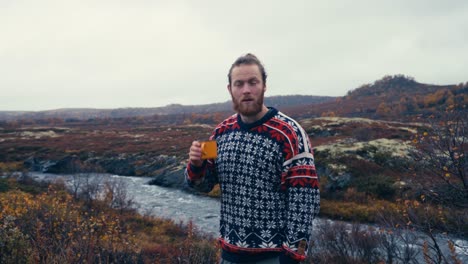Norwegian-Hiker-Drinking-Coffee-Near-The-River-Mountain-At-Dovrefjell-National-Park,-Norway