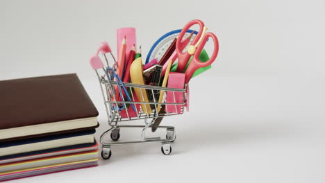 close up of shopping trolley with school items and stack of books on grey background