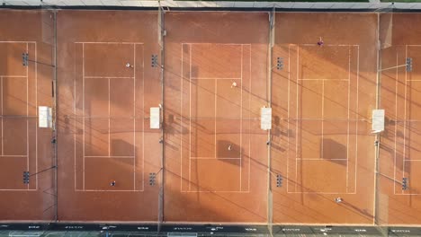 five beautiful clay tennis courts at sunrise filmed with drone, camera down 90 degrees rising, soft light