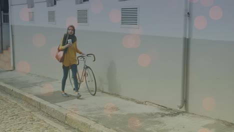 animation of light spots over biracial woman walking with bike