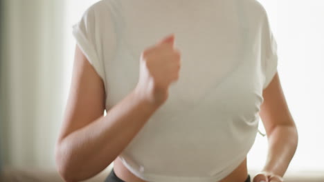 woman runs on trainer at home closeup. slim lady in white top jogs on cardio workout in domestic gym. trained sportswoman enjoys regular exercising