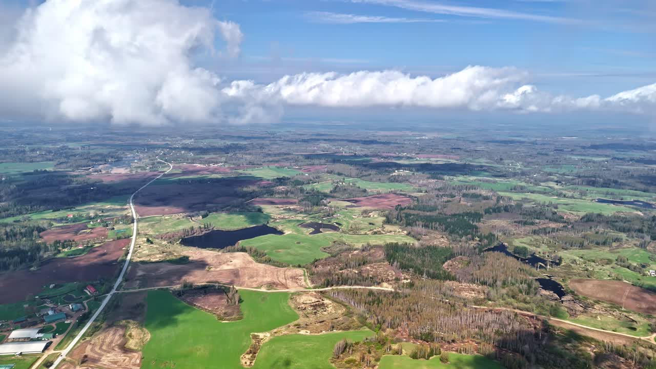 High bird's eye view through the clouds over a rural area with ponds, forests and meadows