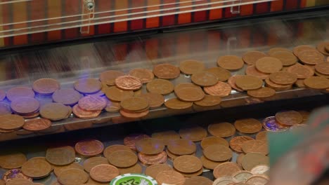 pennies drop onto a shelf coin penny pusher solt machine in an arcade casino