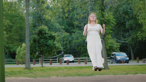 young pregnant woman riding a swing in the park