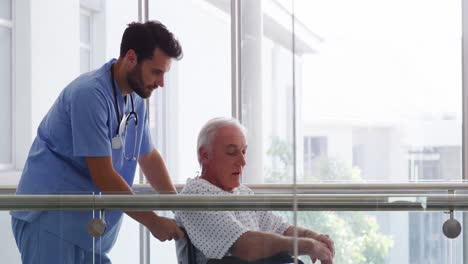 Doctor-holding-senior-patient-on-wheelchair-in-passageway