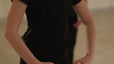 a group of young ballet students in black dancewear practicing positions in a spacious ballet studio with wooden flooring and wall-mounted barres. focused expressions and synchronized movements.