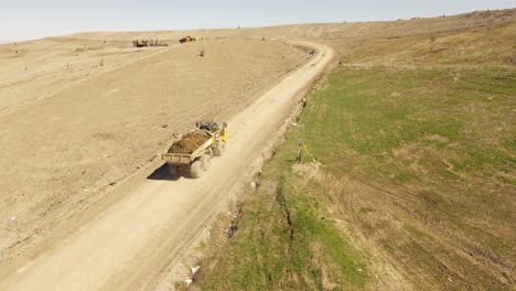 Yellow-heavy-powerful-dump-truck-transport-soil-up-hill,-aerial-drone-view