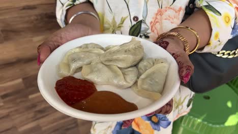 an indian girl holding a plate of veg momo in her hand with heena.