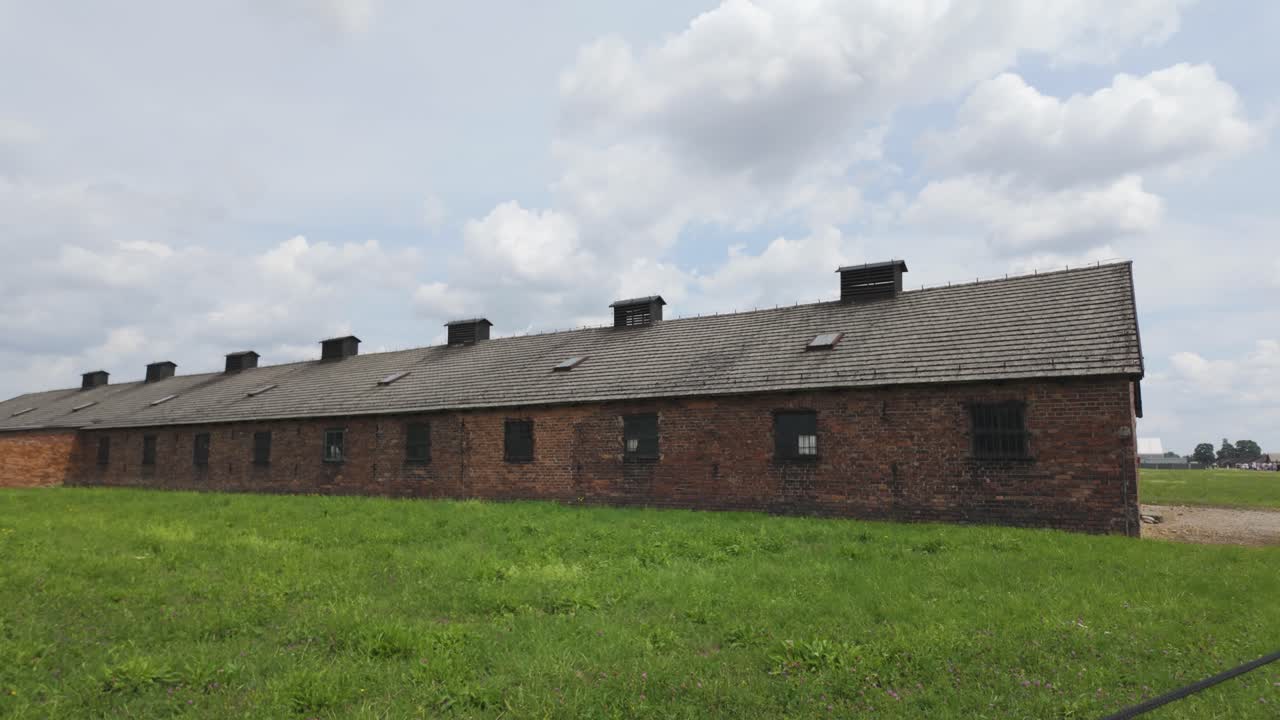 Auschwitz-Birkenau camp barrack under a partly cloudy sky with green grass in the foreground