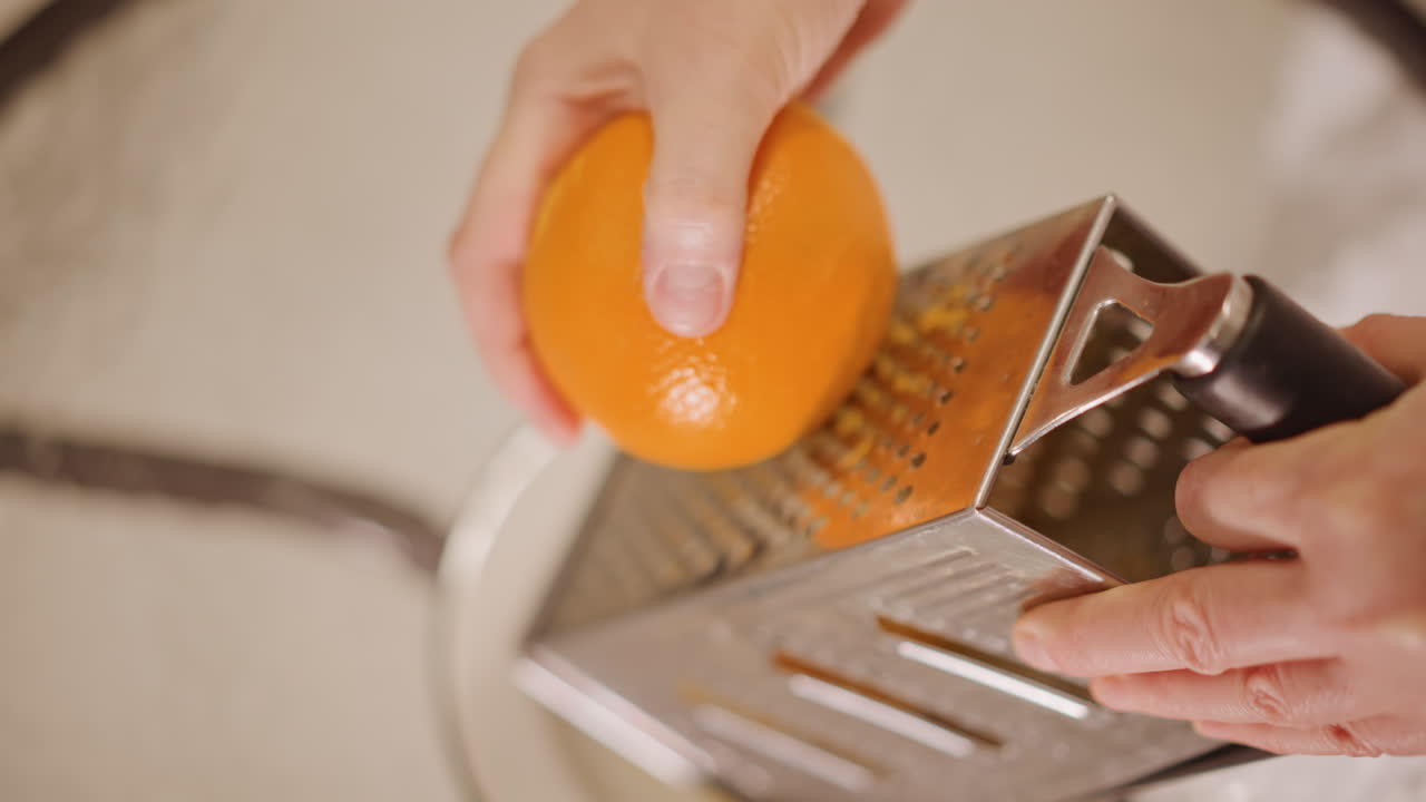 Rallando cítricos para postre. Primer plano de manos rallando cáscara de naranja en un relleno con especias aromáticas. Vista detallada de manos preparando pastel de calabaza con cítricos vibrantes y fragantes especias de otoño.