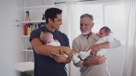 Un-Joven-Hispano-Y-Su-Padre-Mayor-Sosteniendo-A-Sus-Dos-Bebés-En-Casa,-De-Cerca