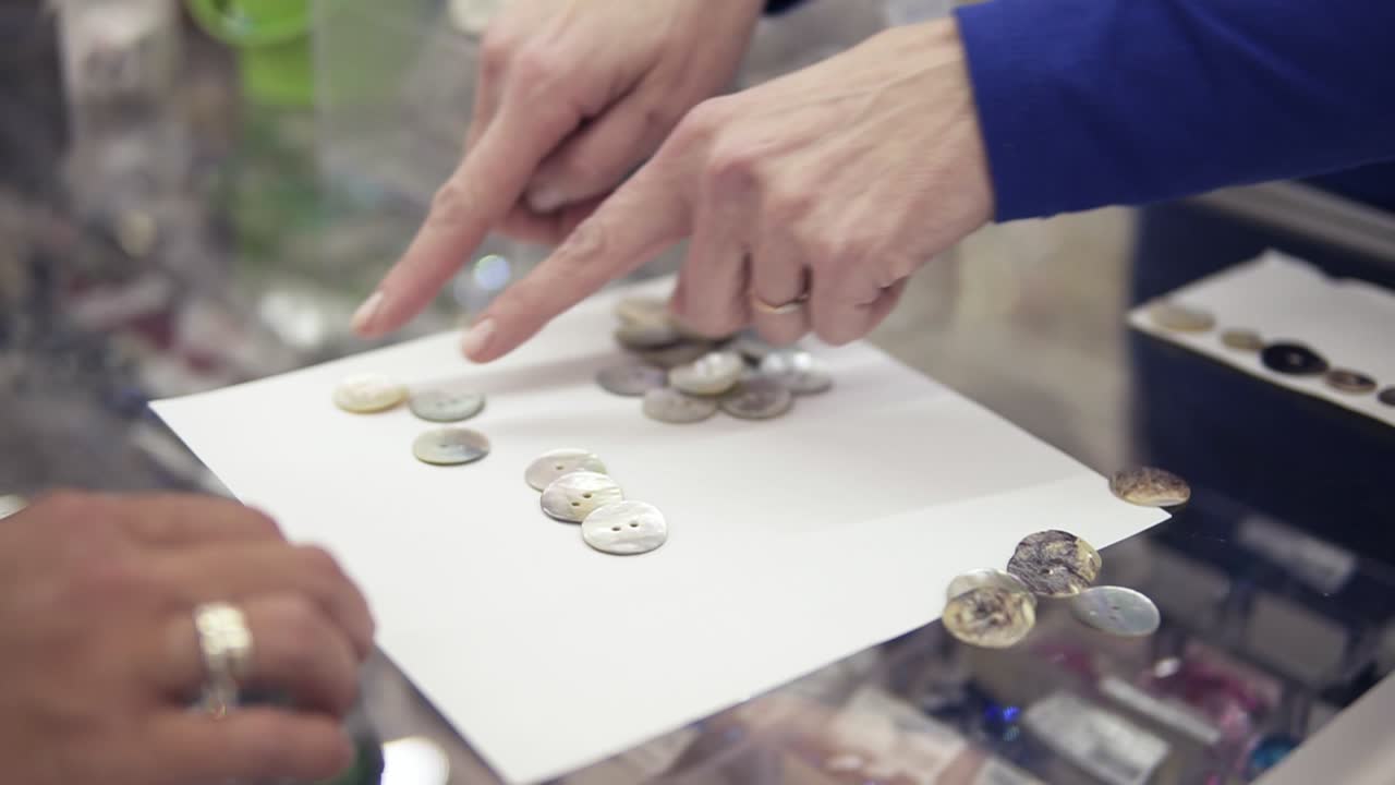 dos mujeres están contando y seleccionando los botones de tela en una mesa de vidrio en una tienda de pañuelos. cliente y vendedor. sólo manos. muy de cerca