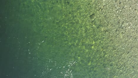 Looking-straight-down-on-a-rippling-river-with-green-and-light-colors