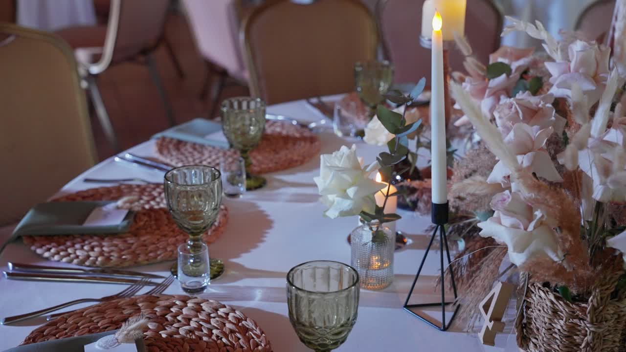 A beautifully arranged dining table adorned with delicate pink roses, lush greenery, and elegant candles. The soft ambient lighting creates a warm, intimate atmosphere
