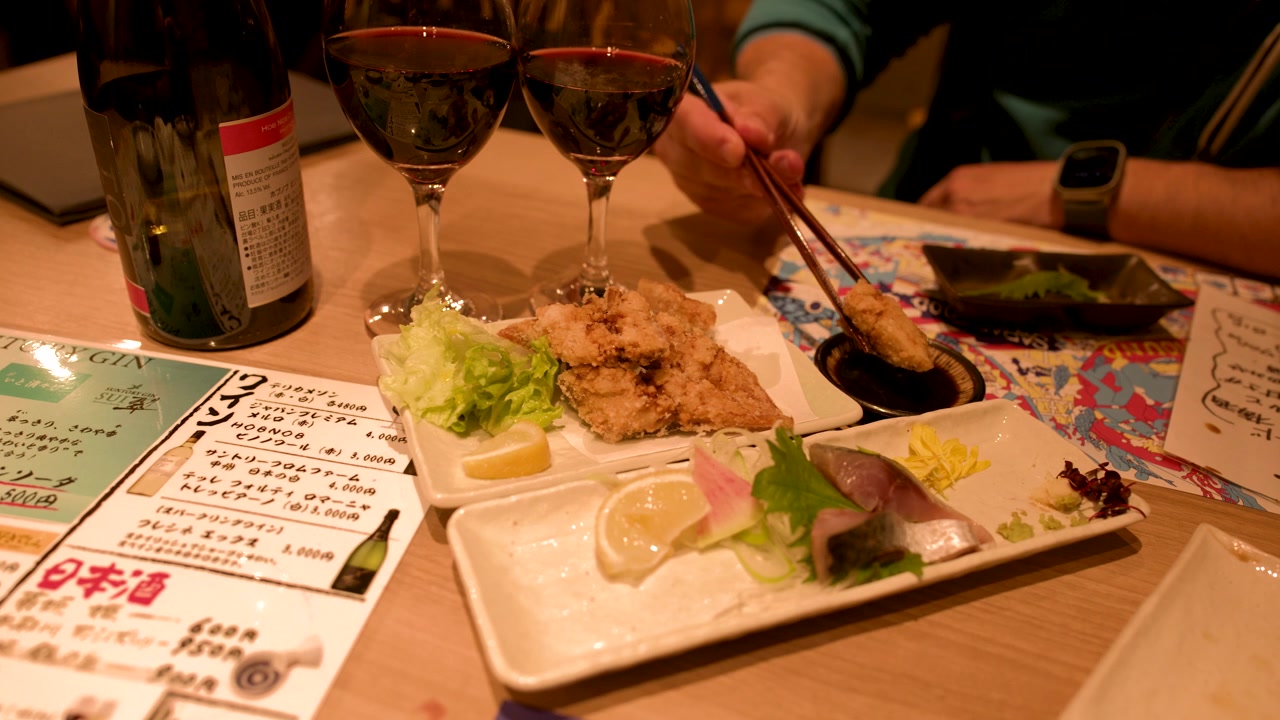 日本食レストランのテーブルで、誰かが箸を使ってフライドチキンをソースに浸している