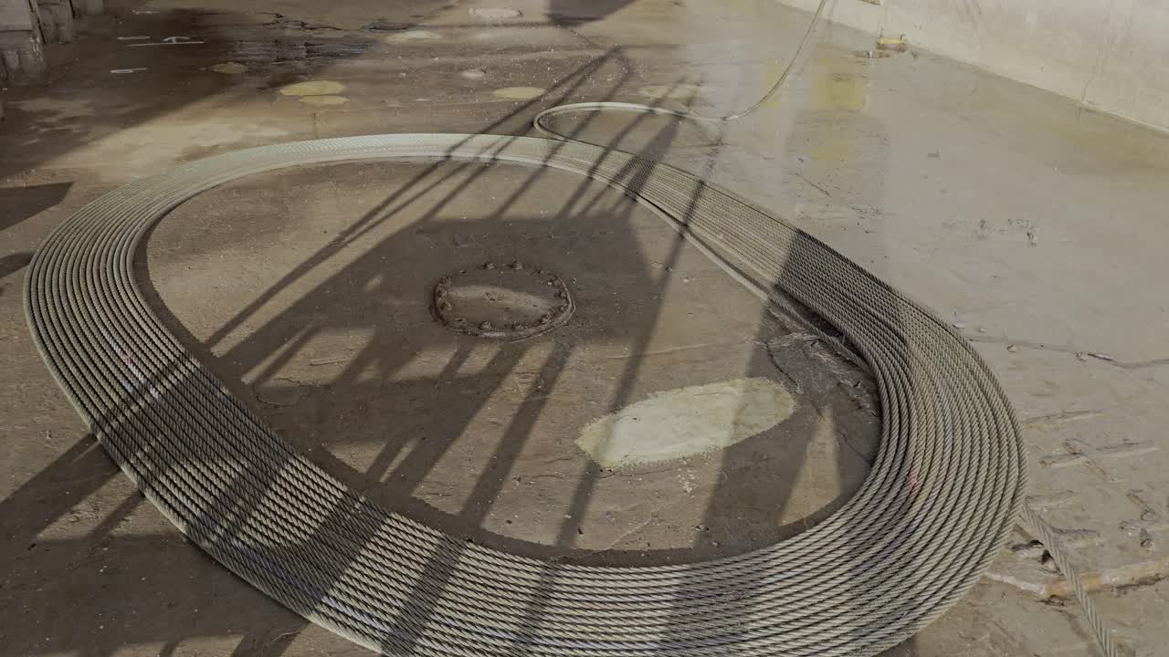 Anchor wire laid out and coiled in neat oval on ground in dry dock, awaiting inspection.